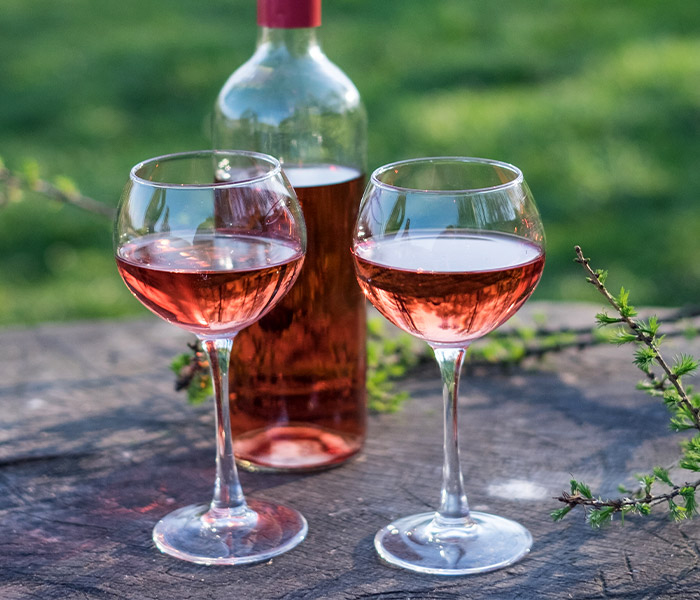 Two glasses of rose wine and a bottle on a rock outside