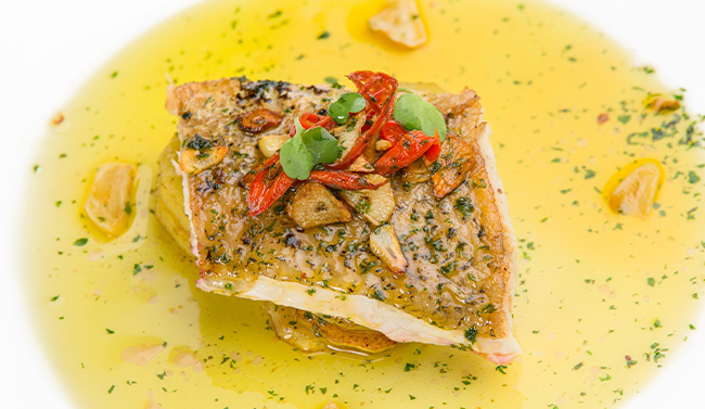 Fish in butter sauce on a white dish with garnishes